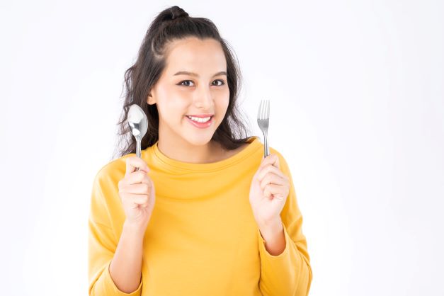 young woman wearing yellow shirt holding spoon and fork
